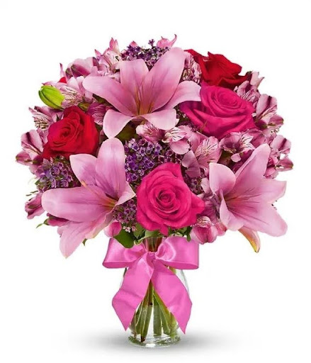 A bouquet of red roses, hot pink roses, pink asiatic lilies, hot pink alstroemeria, filler, ribbon and foliage in a clear glass vase.