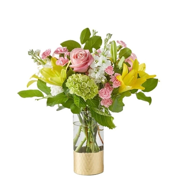 Mixed floral arrangement in glass vase featuring pink roses, yellow lilies, white flowers, and greenery with gold base wrap.