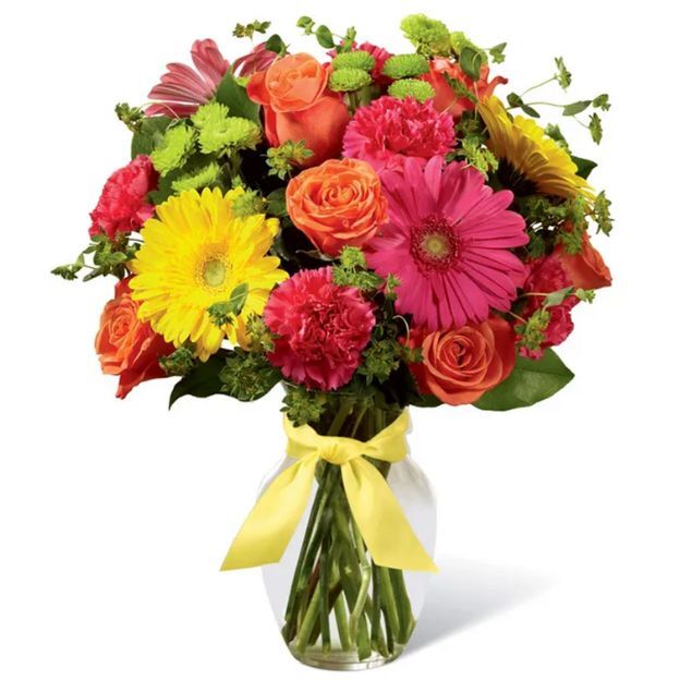 Bright bouquet of pink gerbera, yellow daisy, orange roses, hot pink carnations, green mums in a clear vase with yellow bow.