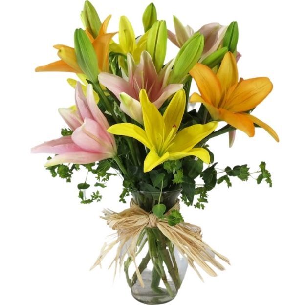 Mixed lilies in yellow, orange, and pink with greenery in a clear vase tied with raffia ribbon.