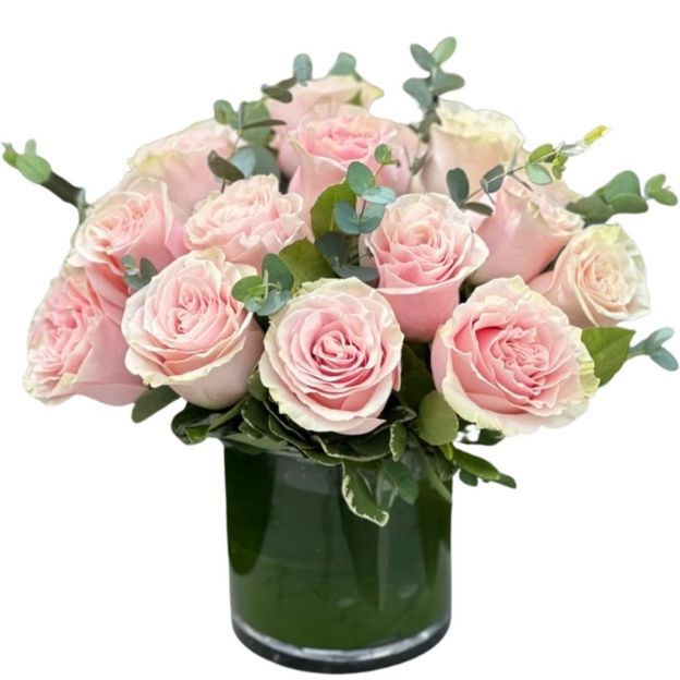 Round bouquet of soft pink roses and variegated greenery in a low glass vase, showcasing romantic, delicate blooms.