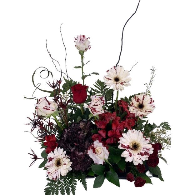 Red and white roses, white daisies with burgundy markings, dark purple blooms, greenery, and tall twisting branches.