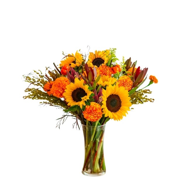 Autumn bouquet of sunflowers, orange marigolds, and red-tipped leaves with stems visible through a clear vase.