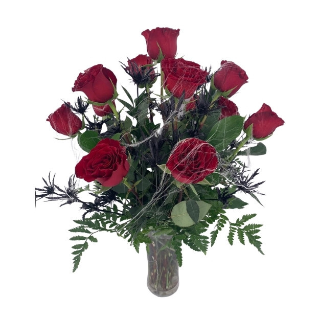 Red roses, black spiky blooms, and green fern leaves draped with wispy cobwebs in a clear glass vase.