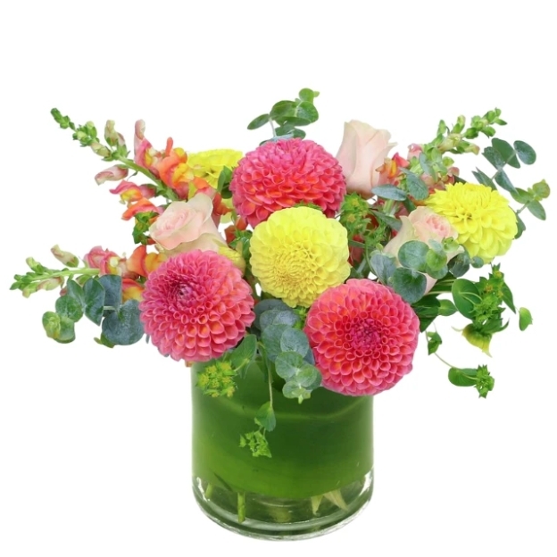 Glass vase arrangement with pink and yellow dahlias, snapdragons, roses, and eucalyptus greenery.