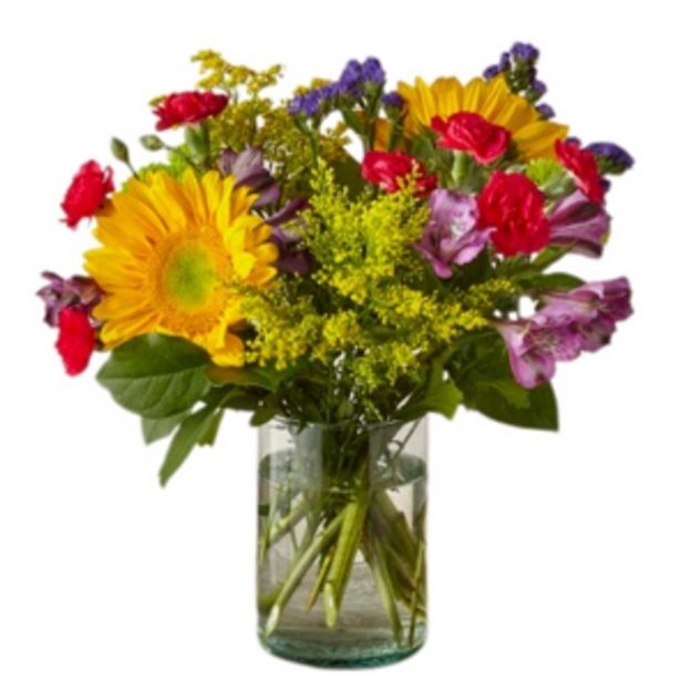 Bright sunflower and red carnation mix with purple alstroemeria and solidago, stems visible in a clear vase.
