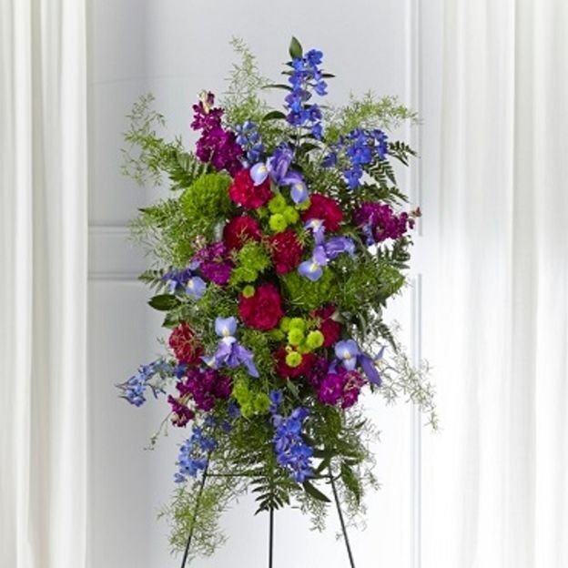 Standing spray with blue delphinium and irises, hot pink roses, and green mums with fern greenery on an easel.