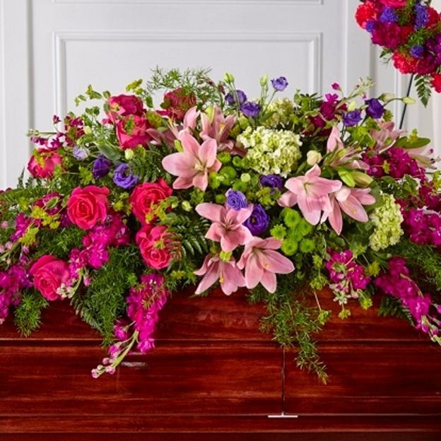 Vibrant casket spray of pink lilies, hot pink roses, purple blooms, and green mums cascading over a mahogany casket.