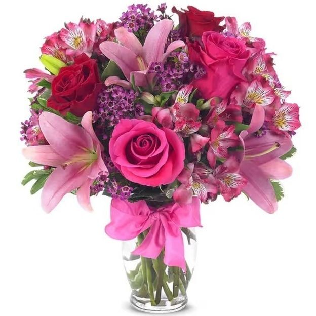 Mixed pink bouquet of lilies, roses, and alstroemeria with purple fillers, tied with a bright pink ribbon.