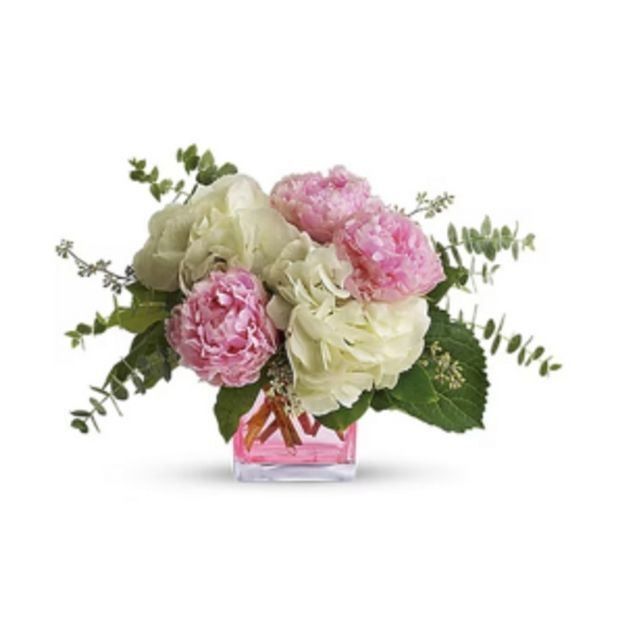 Elegant bouquet of pink and white flowers with lush green leaves in a pink-tinted cube vase.